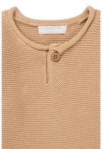 Beige gestricktes Oberteil mit rundem Halsausschnitt, ausgestattet mit einem einzelnen Holzknopf, strukturiertem Stoff und einem Etikett mit der Größenangabe 56 (1-2 Monate).