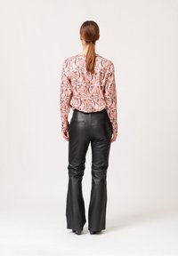 Blusa a maniche lunghe di colore rosa con motivo floreale, abbinata a pantaloni flare in pelle nera, con tasche posteriori visibili e texture liscia.