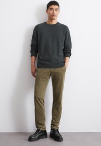 Dark gray knit sweater with a textured pattern, paired with olive green corduroy pants and black shoes, standing against a plain background.