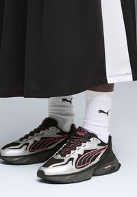 Zwart-grijze sportschoenen met zilveren accenten en roze details. Draagt witte geribbelde sokken met een zwart logo.