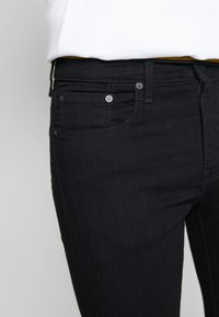 Calças de ganga pretas com um corte justo, apresentando um design de cinco bolsos, fecho com botão padrão e costura tonal discreta.