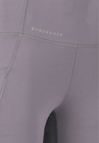 Lila idrottsleggings med en slät textur, med platta sömmar och en reflekterande "ENDURANCE"-logotyp på midjebandet.