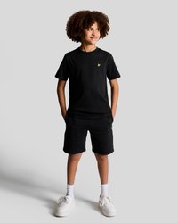 T-shirt noire en coton et shorts, arborant un petit logo jaune. Associés à des baskets blanches et des chaussettes blanches. Coupe décontractée, design simple.