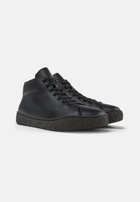 Zapatillas altas negras hechas de cuero liso con una suela de goma negra texturizada. Presentan cordones y costuras visibles a lo largo de las costuras.