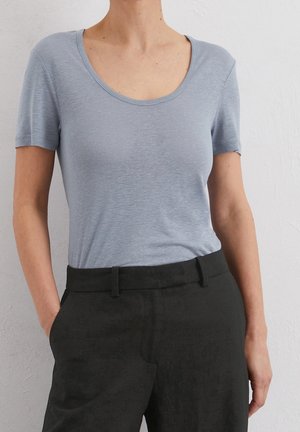 Camiseta azul claro de manga corta con escote redondo, tela texturizada, combinada con pantalones negros de cintura alta con bolsillos delanteros.