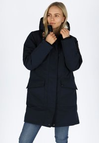 Parka blu navy con cappuccio, foderato in pile, due grandi tasche frontali e chiusure a pressione. Presenta una texture morbida e elementi regolabili.