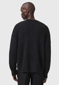 Juodas megztinis, pasižymintis laisvu siluetu, raukšlėtais rankogaliais ir apatine dalimi. Jo tekstūra atrodo minkšta ir stora, atskleidžianti jaukų dizainą.