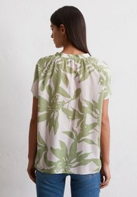 Blouse légère à manches courtes en crème avec un grand motif de feuilles vertes, dotée d'un col froncé et d'une coupe décontractée.