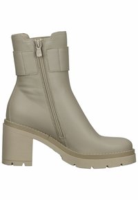 Bottine en cuir beige avec talon épais, fermeture éclair latérale, et large bande décorative autour du haut de la tige, semelle crantée pour une meilleure adhérence.