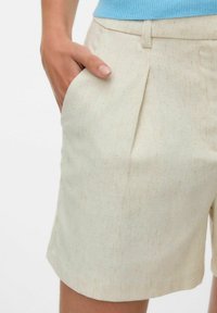 Ljusbeige shorts med en texturerad tyg, med en veck framtill och sidofickor, skräddarsydd passform, och utan synliga detaljer.