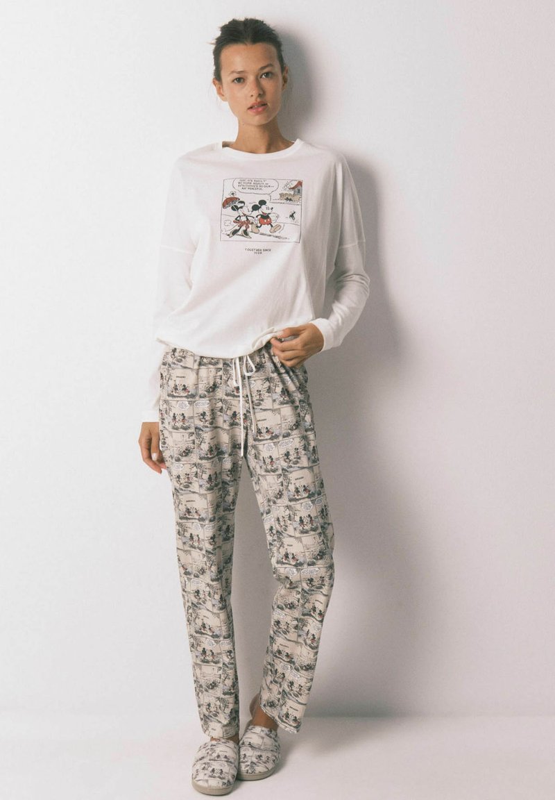 Camicia bianca a maniche lunghe con stampa grafica, abbinata a pantaloni da pigiama a fantasia colorata. Tessuto morbido, vestibilità rilassata, dotata di cintura con cordoncino.