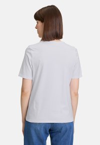 Lichtgrijs katoen t-shirt met een ronde hals en korte mouwen, weergegeven vanuit de achterkant, met een gladde textuur en een eenvoudig ontwerp.