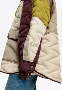Chaqueta acolchada con paneles en verde oliva, burdeos y crema. Incluye detalles de botones y un acabado texturizado.