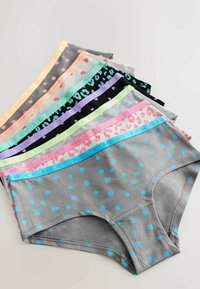 Sept paires de sous-vêtements féminins pliés avec divers imprimés colorés, notamment des pois et des motifs léopard sur un fond clair.