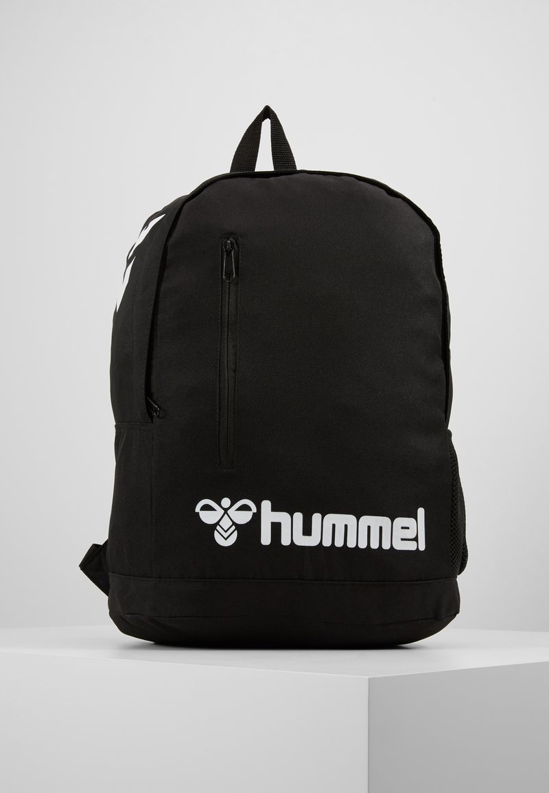 Zaino nero con una texture liscia, dotato di una tasca frontale con zip e del logo bianco "hummel" in basso. Include una maniglia superiore per il trasporto.
