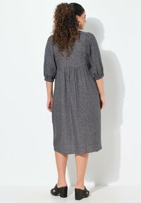 Abito midi grigio con maniche a puff corte, tessuto testurizzato e leggero motivo animalier, vita arricciata, abbinato a tacchi neri.