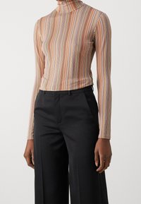Sweter typu golf w cienkiej tkaninie, z cienkimi pionowymi paskami w odcieniach pomarańczowego, zielonego i niebieskiego, zestawiony z czarnymi spodniami w szerokim kroju.