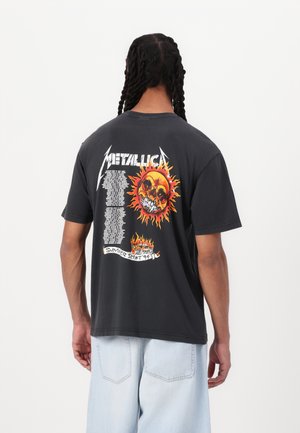 Black cotton t-shirt featuring a graphic print on the back with a skull, flames, and text. Relaxed fit with short sleeves and crew neck.