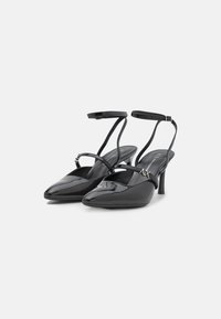 Melnas lakotas ādas slingback kurpes ar smailu purngalu, šauru potītes siksnu un mazu papēdi. Ieroceņi logotipa akcentu uz siksnas.