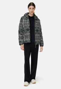 Gepolsterte Steppjacke im schwarz-weißen geometrischen Muster, mit Kapuze, Reißverschluss und oversized Schnitt, kombiniert mit schwarzen Hosen und Sneakers.