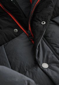 Black and gray quilted jacket featuring a red zipper, silver snap, and smooth texture. Notable stitching accents visible.