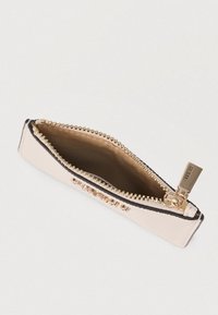 Μπεζ λεπτό τσαντάκι με φερμουάρ και χρυσό μεταλλικό φερμουάρ, με λεπτομέρεια το λογότυπο GUESS, εμφανιζόμενο ανοιχτό με ορατή καφέ υφασμάτινη επένδυση εσωτερικά.