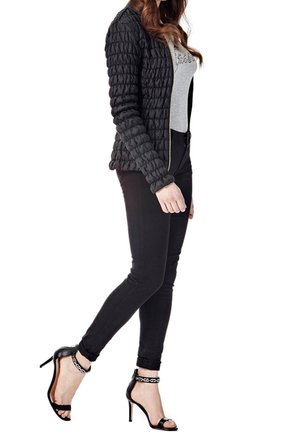 Giacca nera trapuntata con chiusura a zip, indossata sopra una t-shirt grigia. Abbinata a jeans skinny neri e sandali con tacco alto neri.