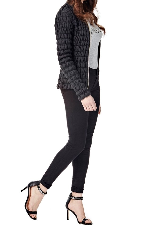 Giacca nera trapuntata con chiusura a zip, indossata sopra una t-shirt grigia. Abbinata a jeans skinny neri e sandali con tacco alto neri.
