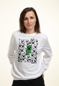 Felpa bianca con una stampa grafica di personaggi a blocchi verdi e neri su uno sfondo bianco e nero di volti quadrati.