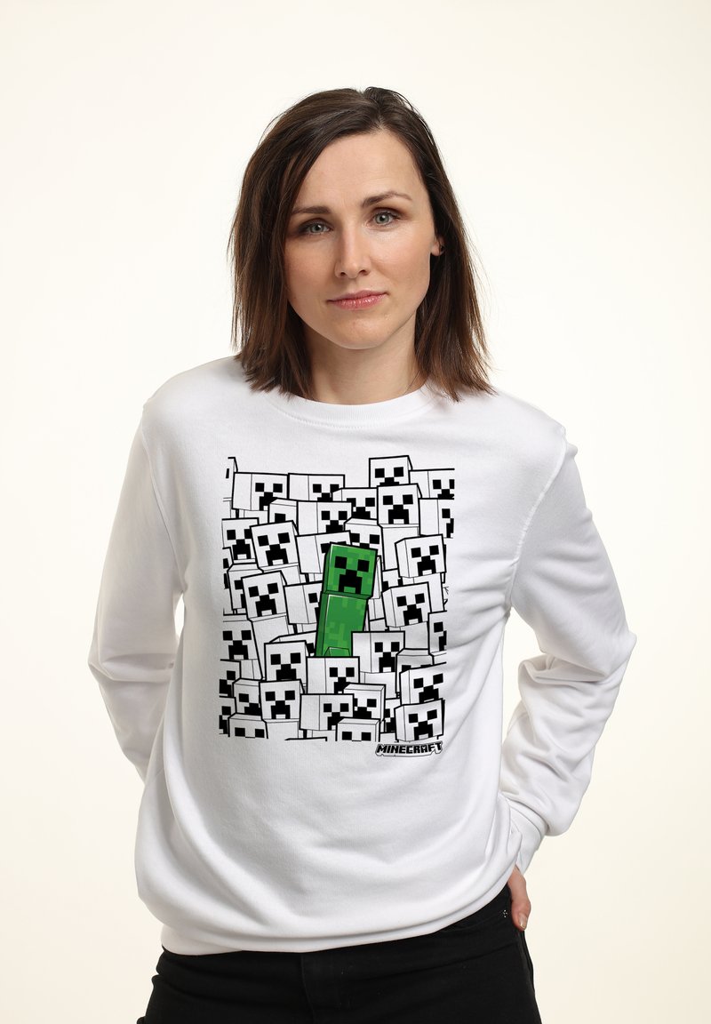 Bílá mikina s grafikou znázorňující zelené a černé blokové postavy na bílém a černém pozadí se čtvercovými obličeji.