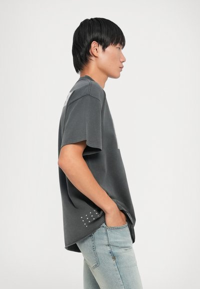 Grijze katoenen t-shirt met korte mouwen, voorzien van een zak en een klein wit sterrenpatroon dichtbij de zoom, gecombineerd met lichtblauwe jeans.