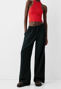 Top corto a rete rossa con bretelle, abbinato a pantaloni larghi neri con vita elastica e coulisse. Sandali neri con una fibbia circolare.