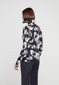 Long-sleeve black turtleneck with white floral pattern. Stretchy fabric, fitted design. Smooth texture, sleek silhouette, subtle detailing.