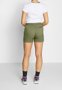 Gröna bomullsshorts med elastisk midja, som bärs tillsammans med en vit t-shirt. Svarta strumpor och flerfärgade sneakers syns också.