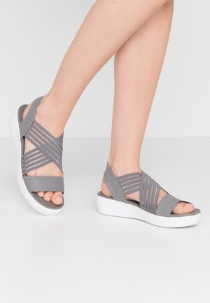 Sandalias grises con tiras elásticas cruzadas. Suela plataforma blanca. Diseño de dedo abierto con textura suave y estilo minimalista.
