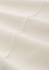 Cremefarbenes Gewebe mit glatter Textur, das subtile Falten und ein gleichmäßiges Webmuster aufweist und dadurch seine Weichheit und Qualität betont.