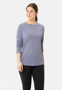 Blaues Langarmoberteil mit Rundhalsausschnitt und Raglanärmeln, aus leichtem, strukturiertem Stoff, kombiniert mit schwarzen, enganliegenden Hosen.