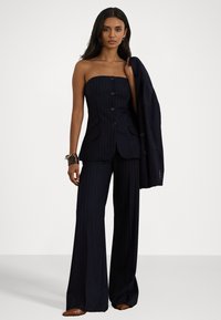 Strapless pinstripe suit in navy, met een getailleerde bodice met knopen, wijde broekspijpen, en een bijpassende blazer die over één arm hangt.