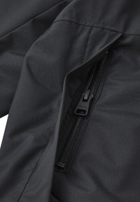 Czarna tkanina o gładkiej fakturze posiada kieszeń na zamek błyskawiczny. Zamek jest matowy, czarny, umieszczony pionowo, zintegrowany z materiałem.