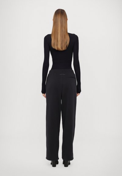 Svart långärmad åtsittande topp kombinerad med vida svarta byxor. Byxorna har dragsko i midjan och bakfickor. Slät textur.