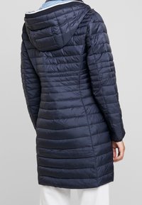 Marineblå puffjakke med et struktureret, quiltet design. Har hætte, lange ærmer og lynlås. Glat, shiny stof.