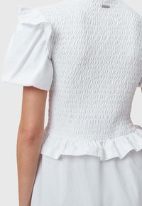 Vestido blanco con corpiño fruncido, mangas cortas abullonadas y un dobladillo con volantes. Hecho de una tela ligera con una superficie texturizada.