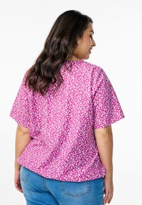 Camicetta a maniche corte in tessuto rosa con un motivo floreale bianco, caratterizzata da una vestibilità rilassata e orlo curvato. La vista posteriore mostra una leggera texture.