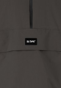 Grå vindjakke med halv-lynlås design, der har en vandret lomme og et rektangulært sort label, der står "SLOPE."