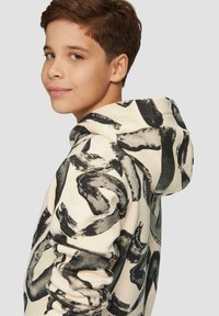 Felpa con cappuccio color crema con un audace motivo astratto in nero. Presenta una vestibilità comoda, tessuto morbido e cuciture visibili lungo le giunture.