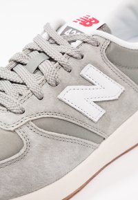 Baskets New Balance grises avec logo blanc, lacets gris, tige en suède et mesh, et marquage rouge sur la languette.