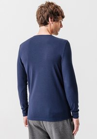 Camicia a maniche lunghe di colore blu navy con scollatura rotonda, morbida al tatto e dal design aderente, abbinata a pantaloni grigio chiaro. Nessun logo o motivo visibile.