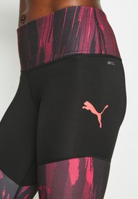 Černé sportovní legíny s růžovým a fialovým vzorovaným pasem, logem DryCell a růžovým logem Puma na stehně. Design z pružné látky.