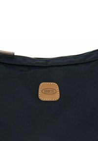 Borsa da viaggio in nylon nero con una patch in pelle marrone e cuciture beige, dotata di chiusura con zip lungo il bordo superiore.