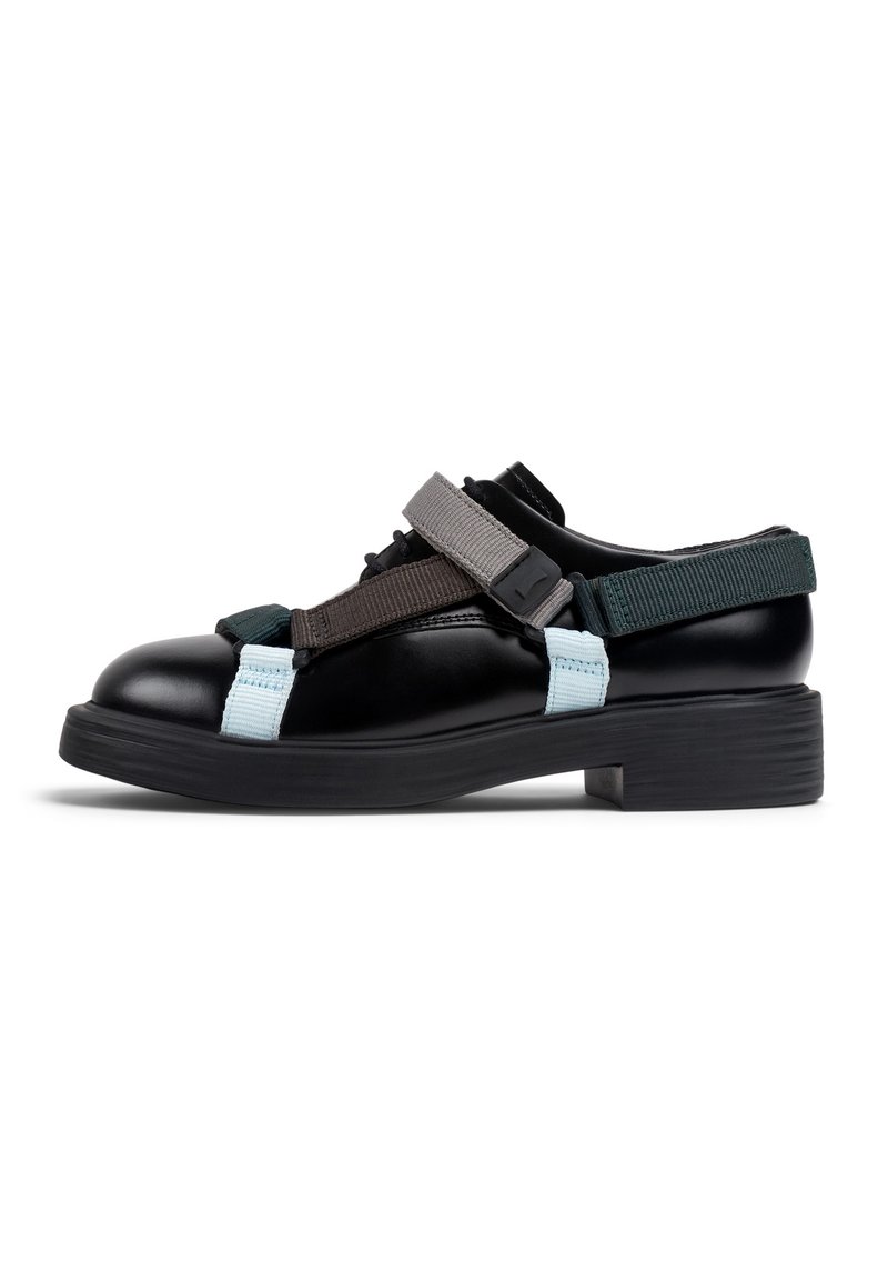Zapatos de cuero negro con una suela gruesa, que cuentan con correas elásticas en gris, verde oscuro y azul claro en la parte superior y los lados.